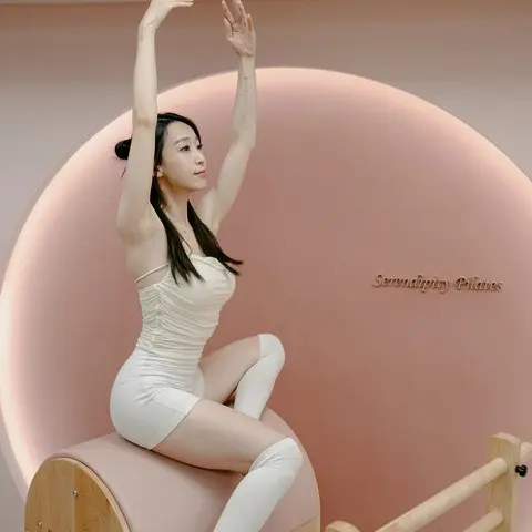 學員身穿白色練習服，在粉色圓形光牆前雙手向上延伸，做開展伸展